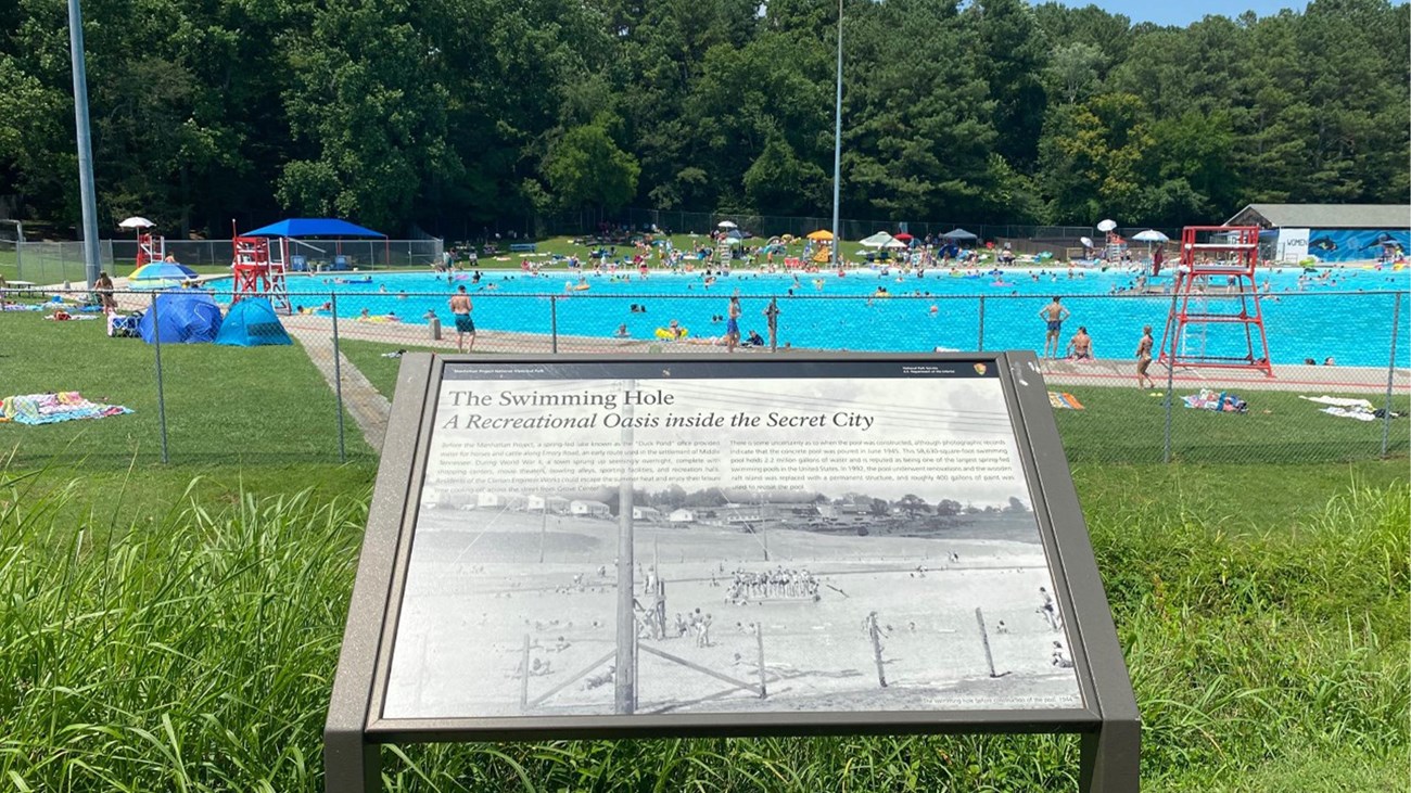 A wayside exhibit in the foreground of a large public pool.