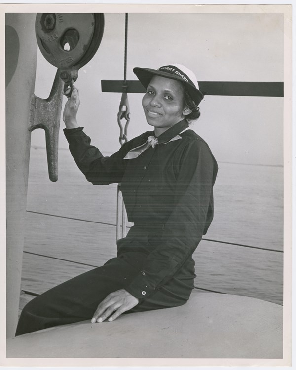 African American woman in military uniform seated on the deck of a ship smiling at the camera