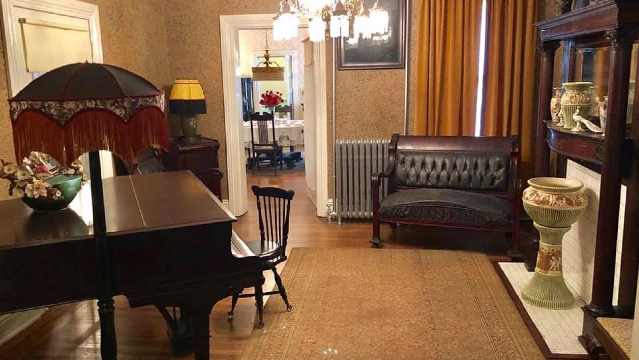 The parlor room with a tall lamp, baby grand piano, couch and vase surrounding the room