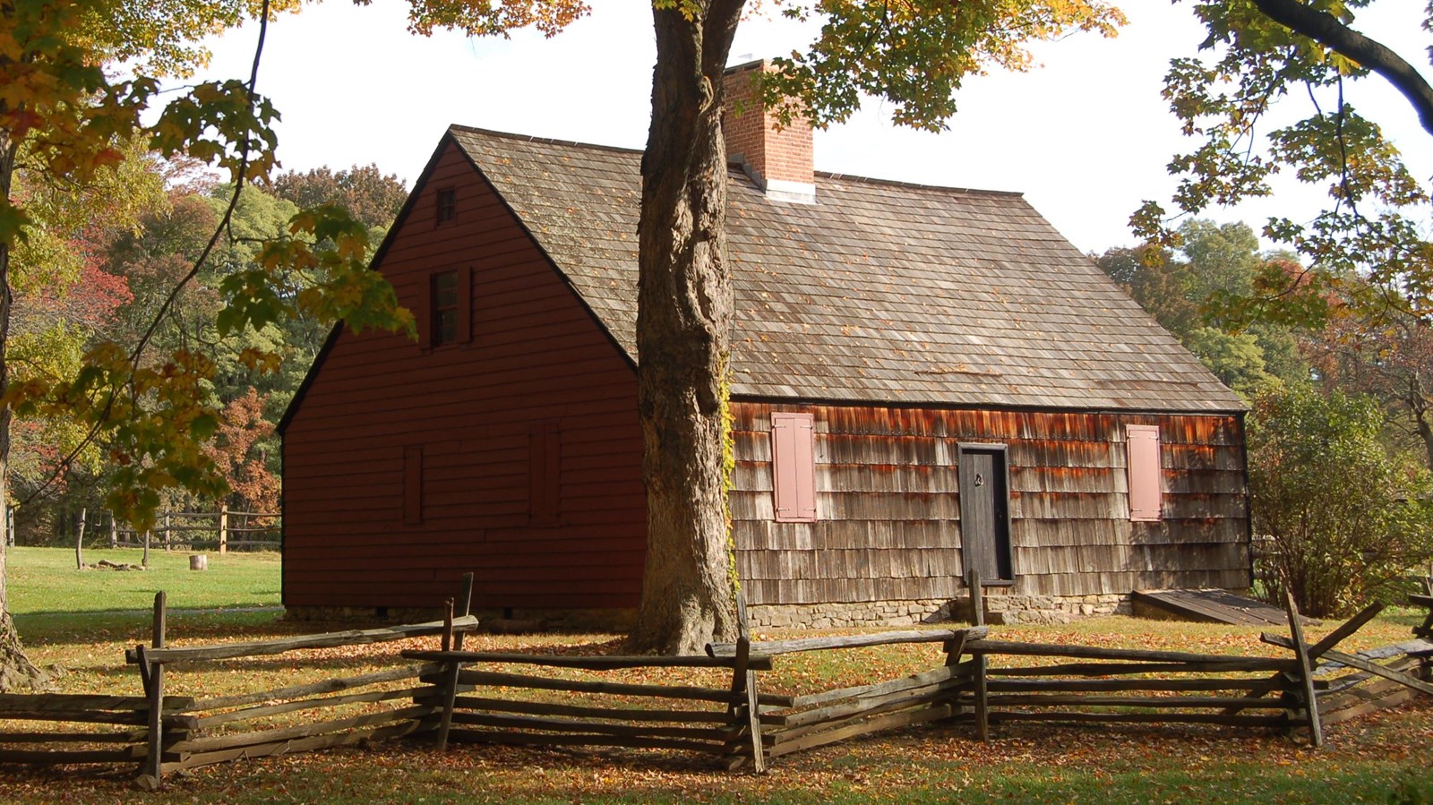 A colonial farm house with a brick chimney and split rail fence around the house