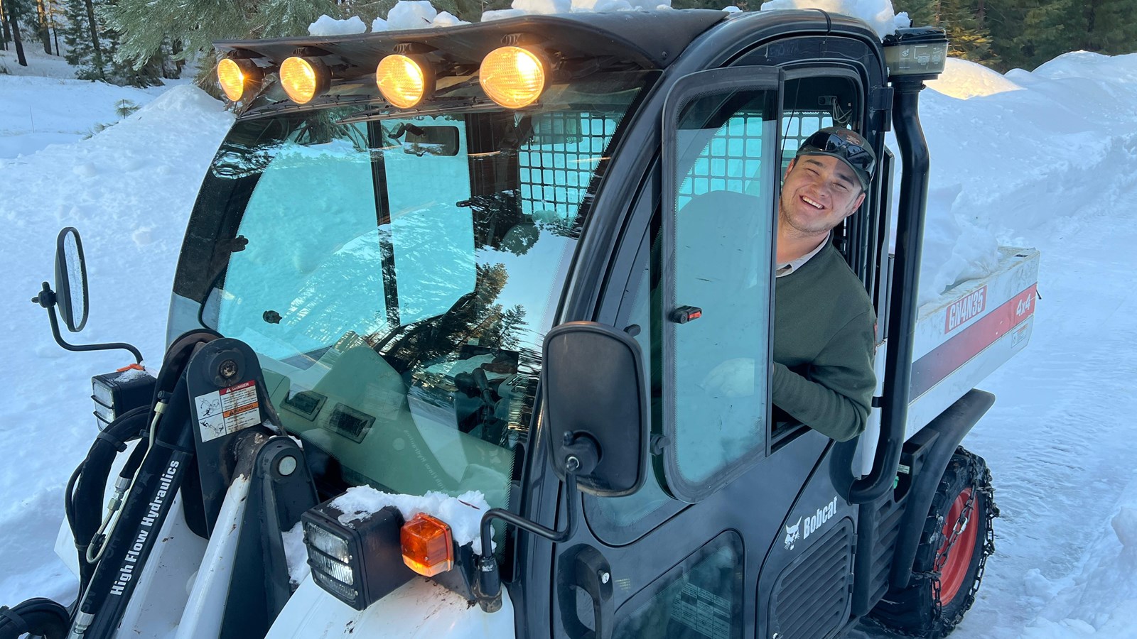 A park ranger drives a snow-clearing ATV on a wooded trail.