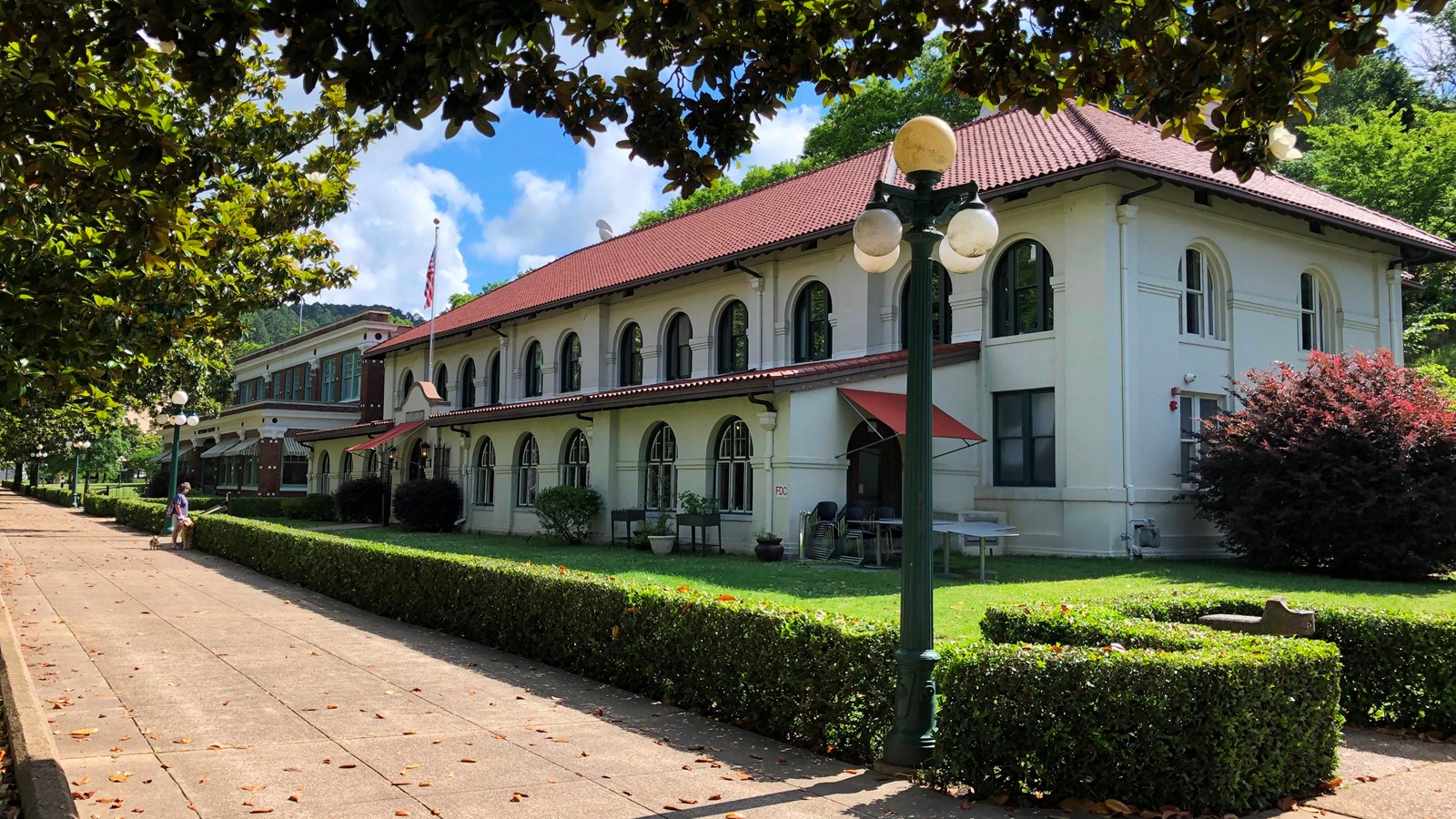 A white stucco building with a red tiled roof sits behind a short, long green hedge.