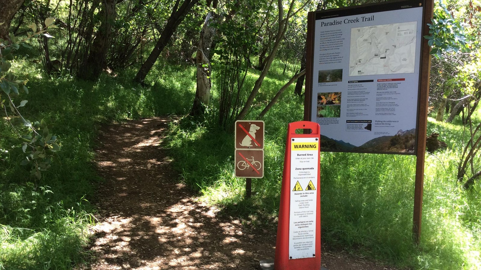 a trailhead sign a burned area warning sign are located at the beginning of a trail.