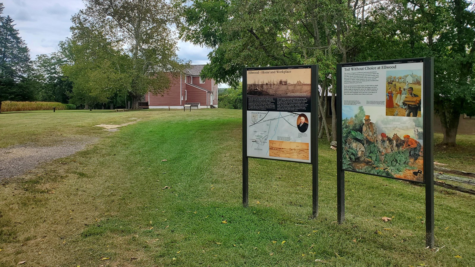 Two upright signs about Ellwood in front of a lawn leading to a historical house.