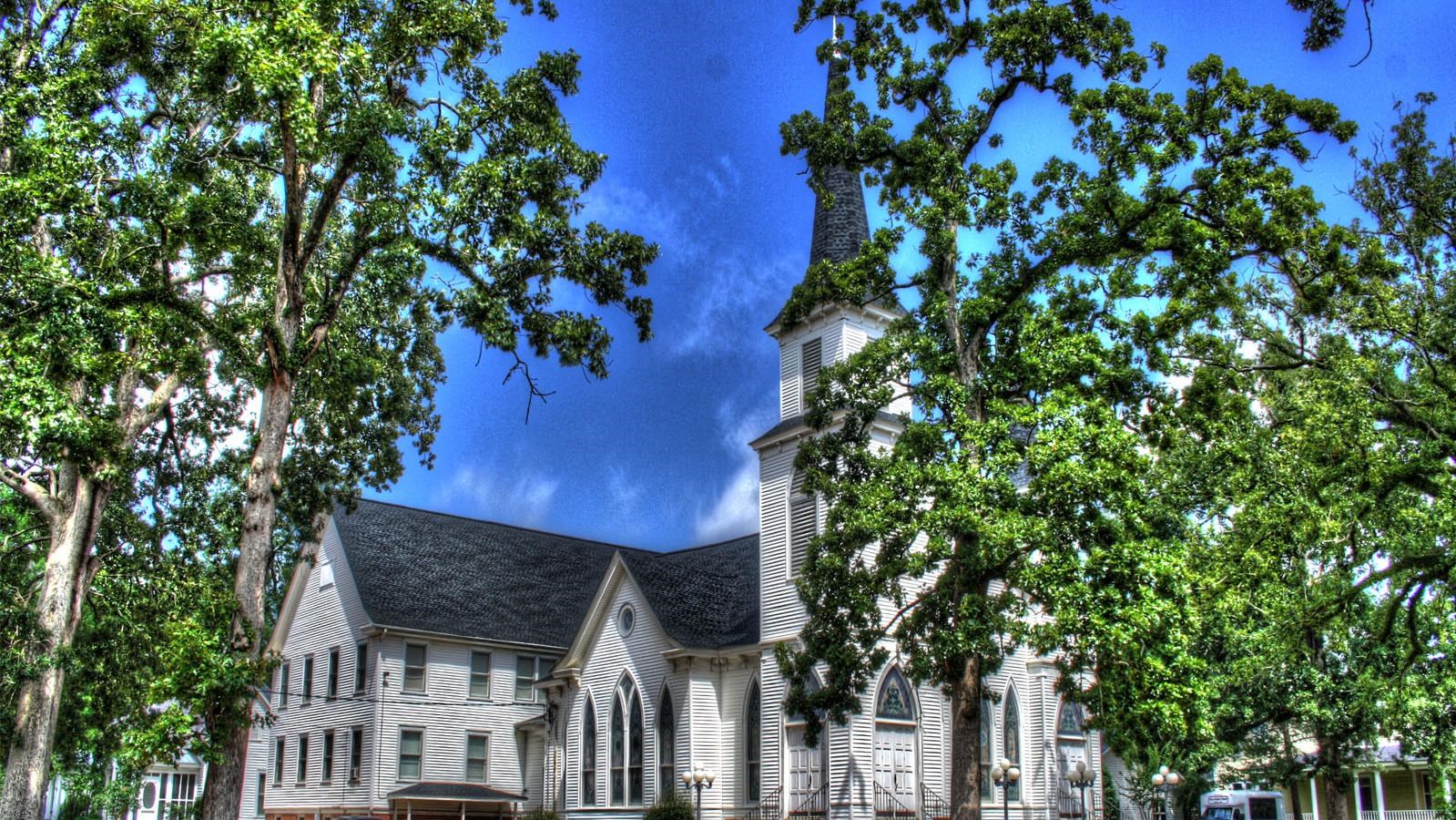 a white clapboard building rises from a red dirt parking lot
