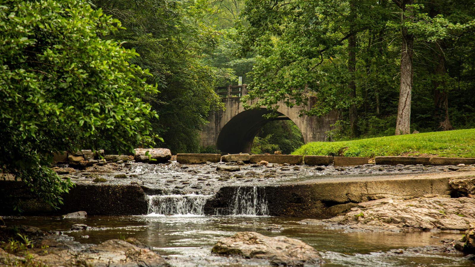 A creek flowing over rocks with a cement bridge in the distance 