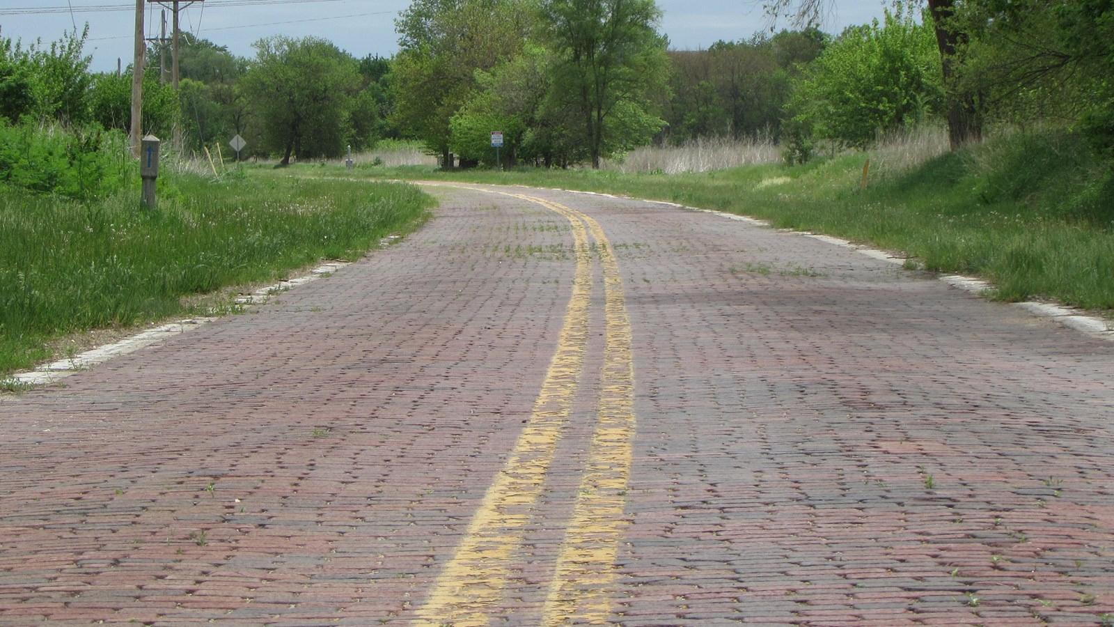 Brick paved road, double-yellow stipes, no shoulders, rural setting.