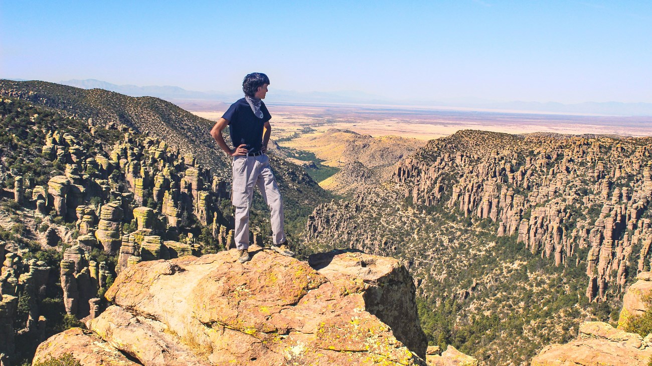 hiker stands on a rock over a dramatic valley of rock formations