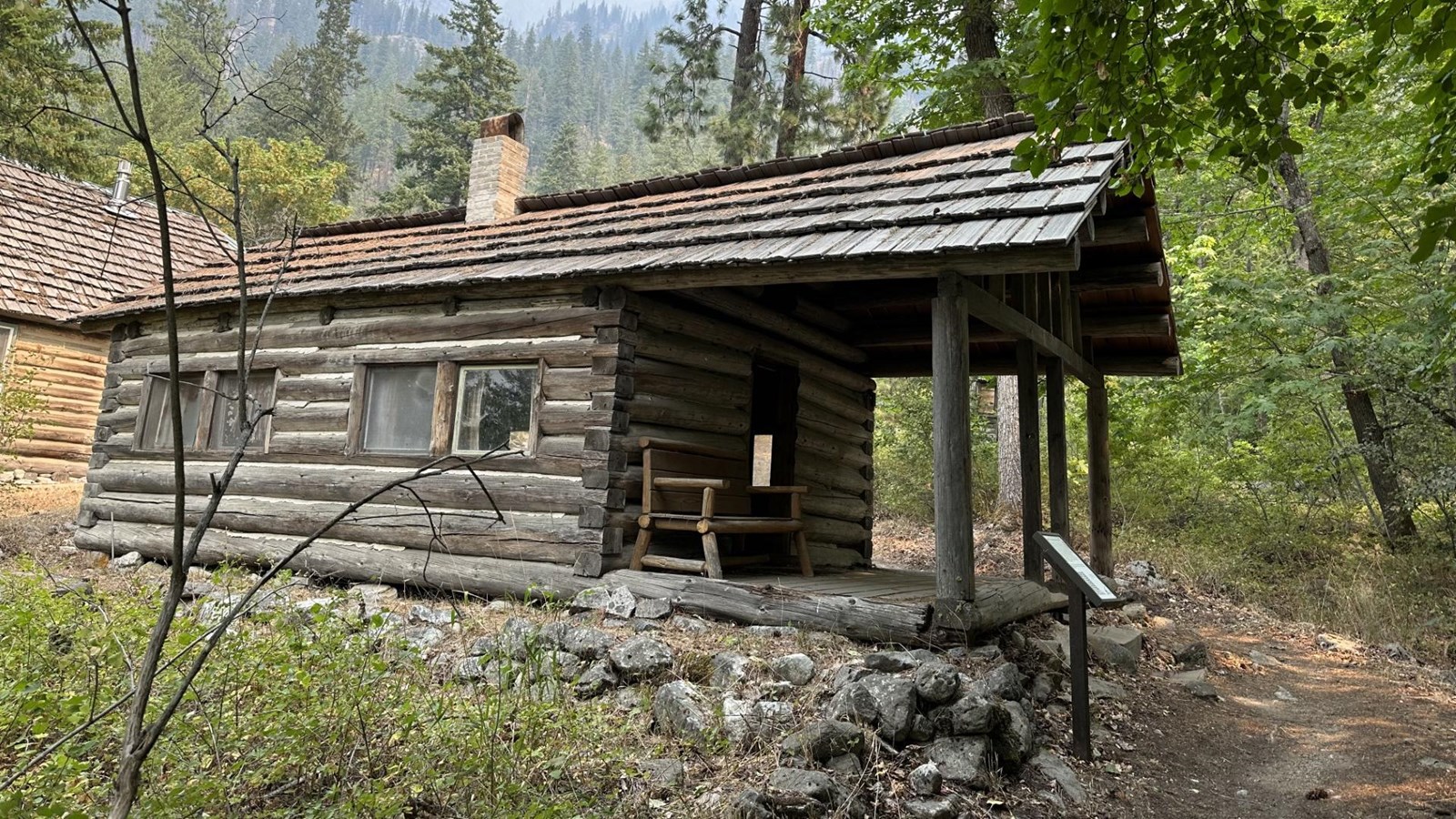 A small cabin with large covered front forch sits in a woodland