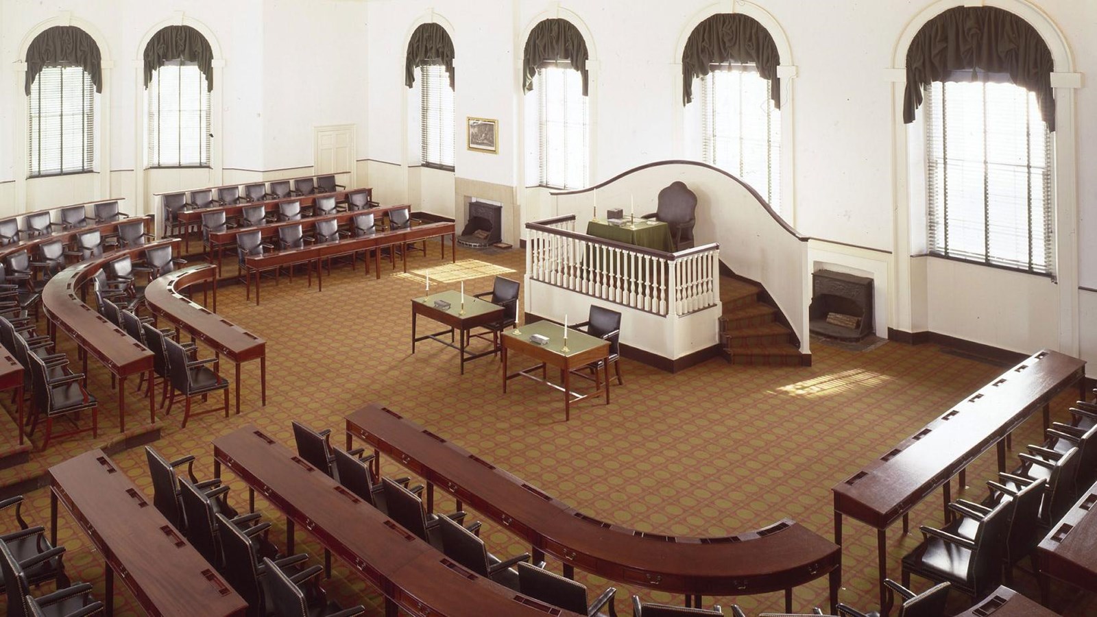 Large room with carpet, three rows of dark chairs, center podium