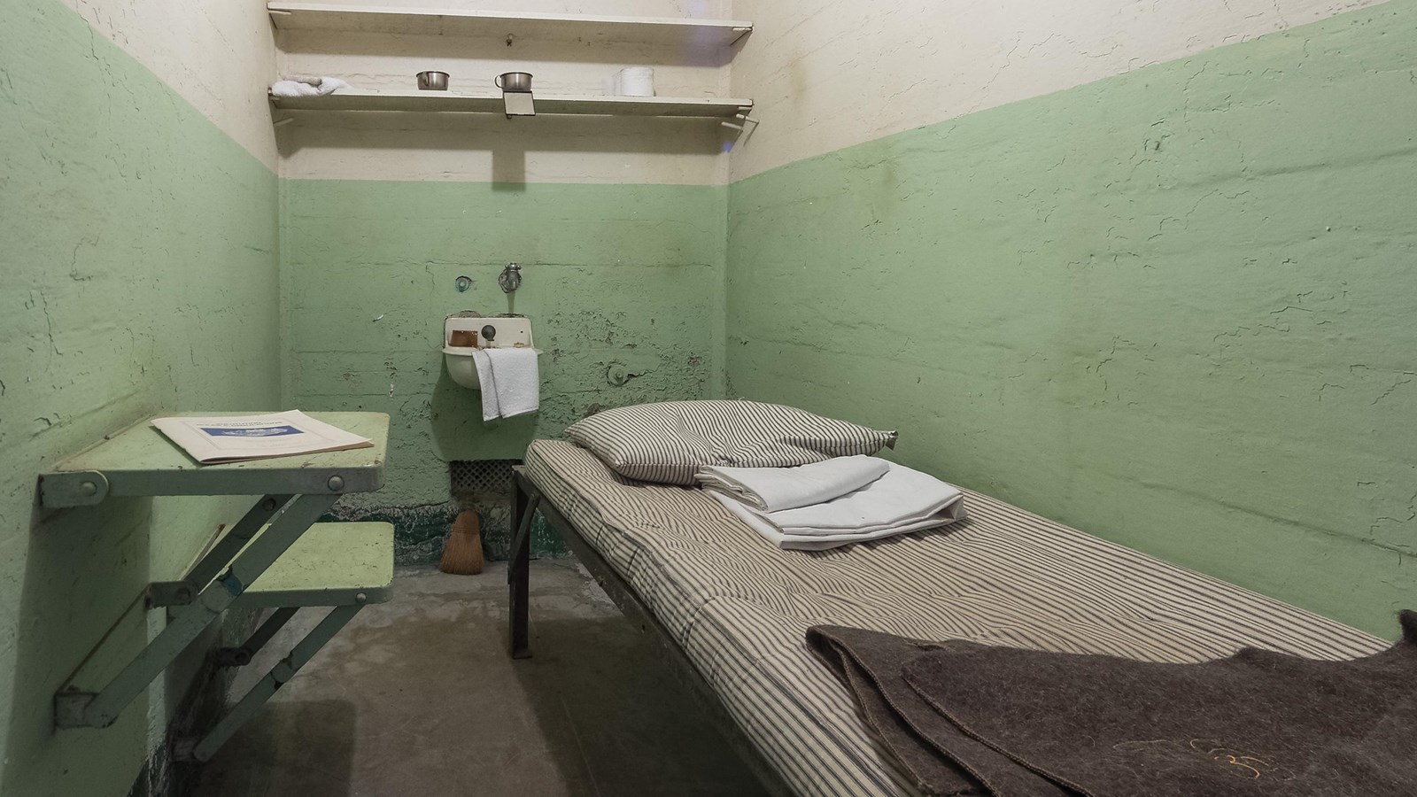 A bare prison cell with a toilet, a sink, and a bed. 