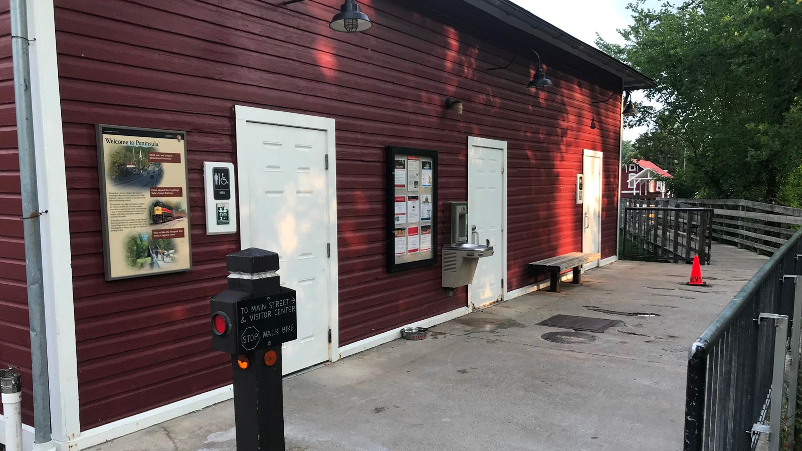 A panel on the outside wall of a red one-story building with white trim, left of two restroom doors.