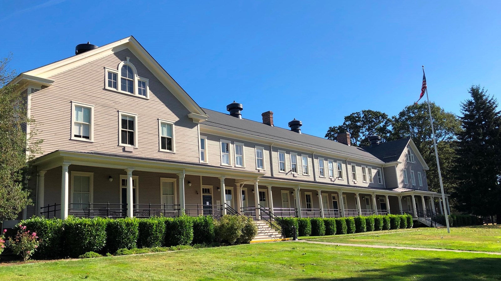 A long building, painted beige, with an American flag on a flagpole in front.
