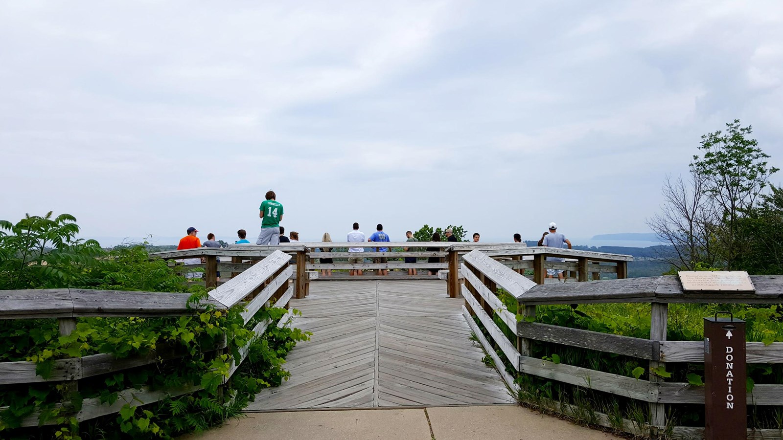 Wooden ramp leads to wooden platform with people looking toward lake and dunes