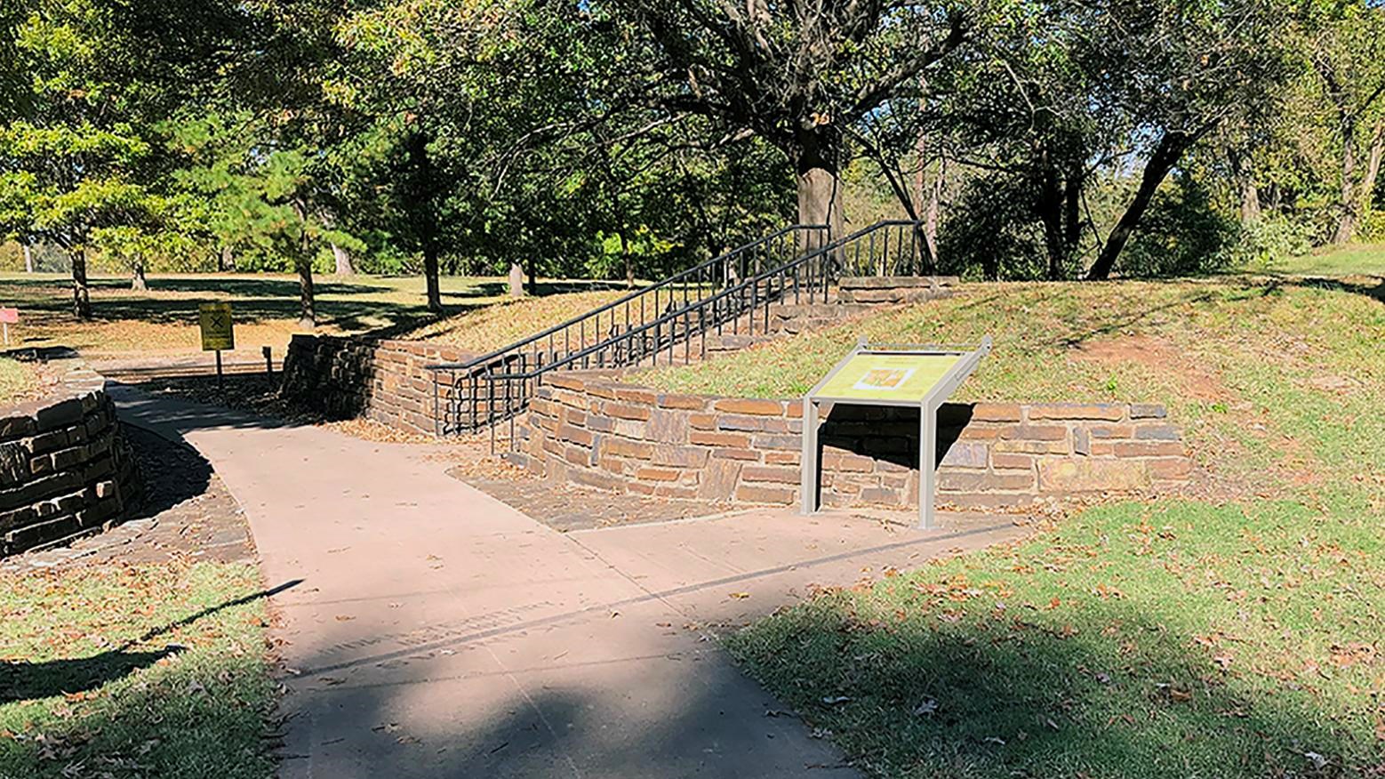 Sidewalk between two dark stone retaining walls. Wayside is on the right just past a black line. 