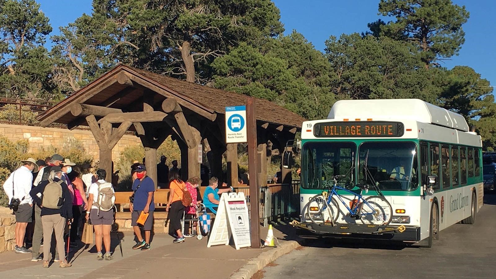 People boarding a large shuttle bus at a bus stop with an rustic, open-air shade structure and 