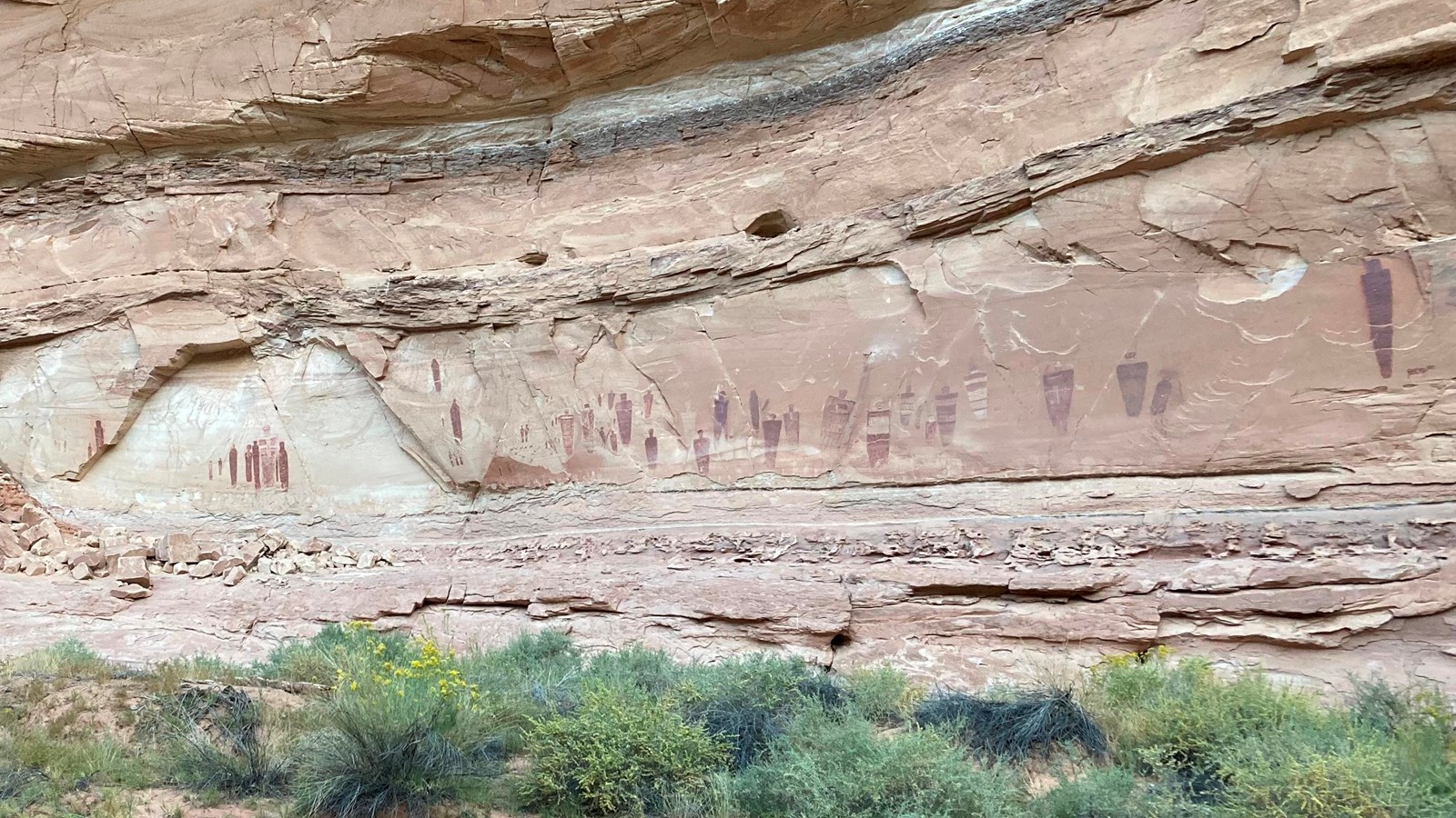 painted person-like figures in red and brown on a long sandstone wall