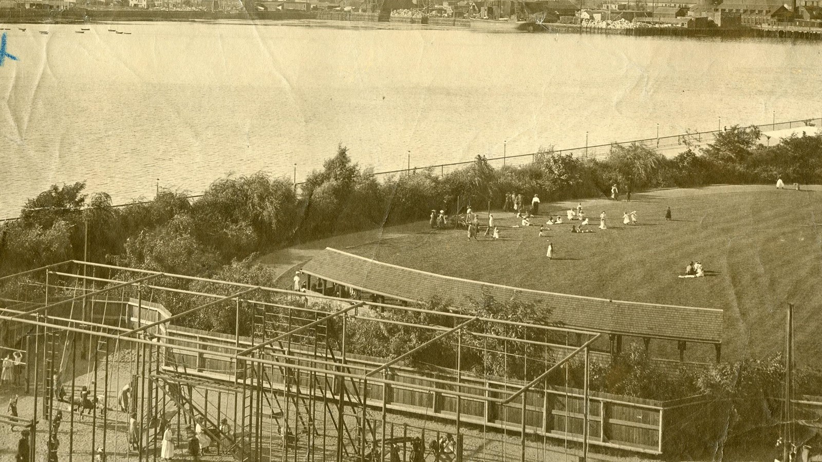 Black and white of large grassy area next to water and a playground next to it 