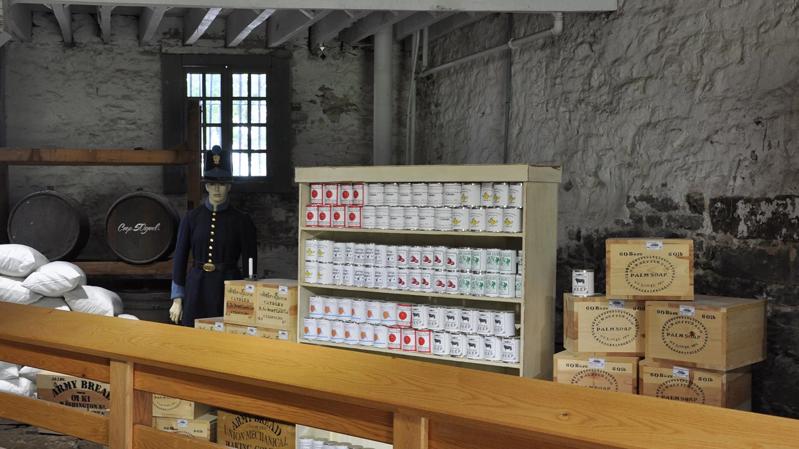 A mannequin in dark blue uniform stands next wooden supply boxes and shelves of canned goods.  