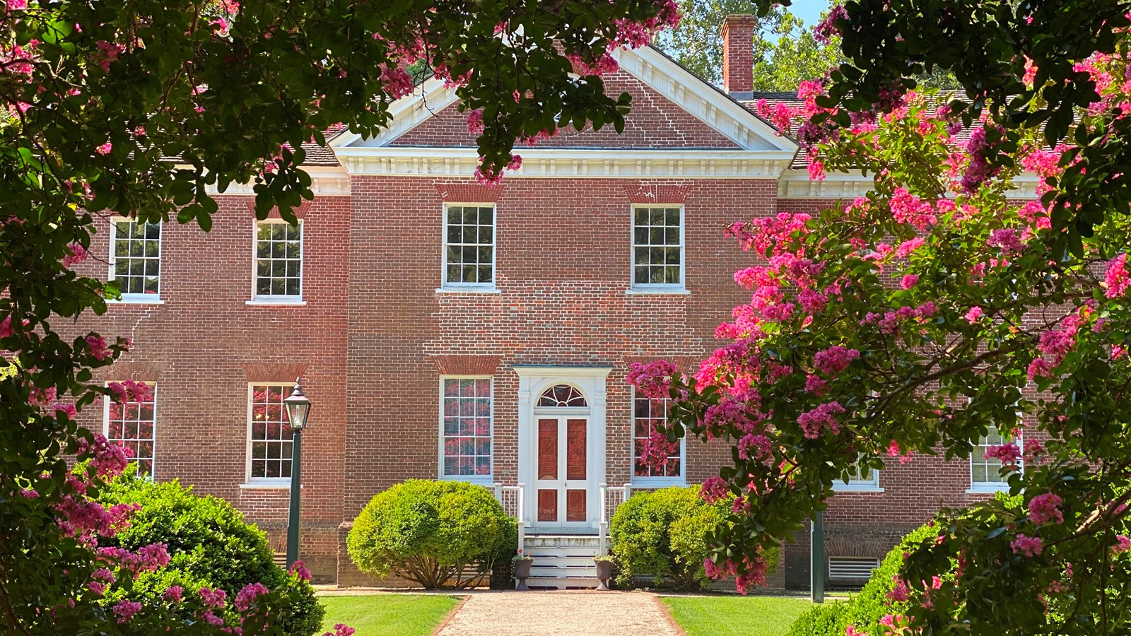 A historic brick house surrounded by blooming pink flowers.