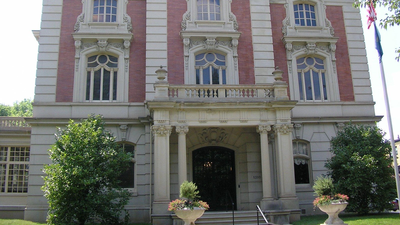 Exterior view of a two-story white and red stone building with an ornate columned porch