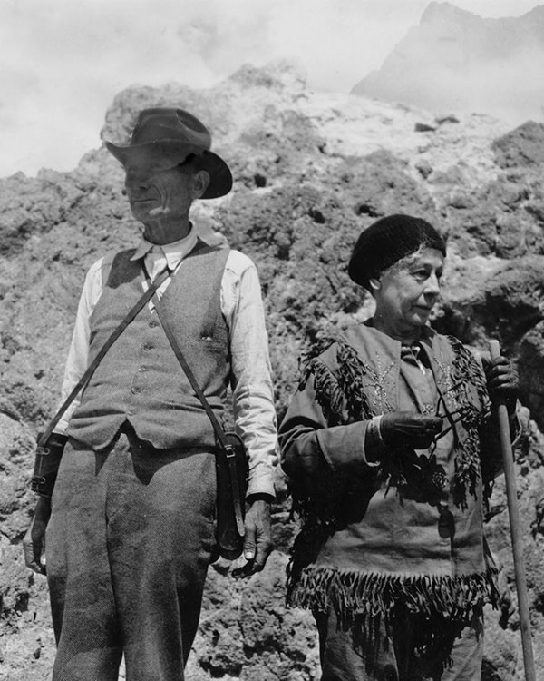 A black and white photo of a man and a woman standing on a volcanic peak.