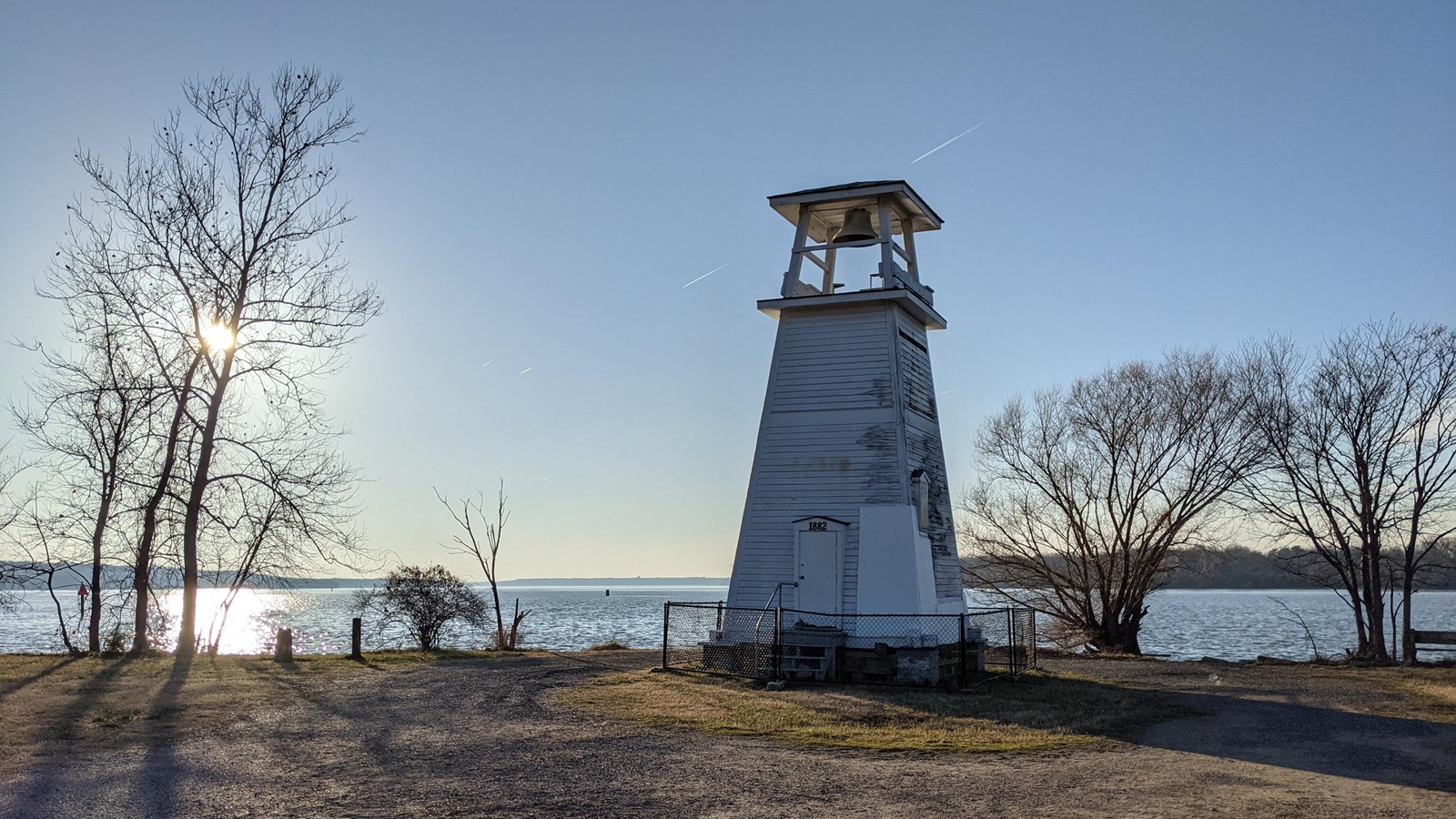 a small white lighthouse stands on the river\'s shore