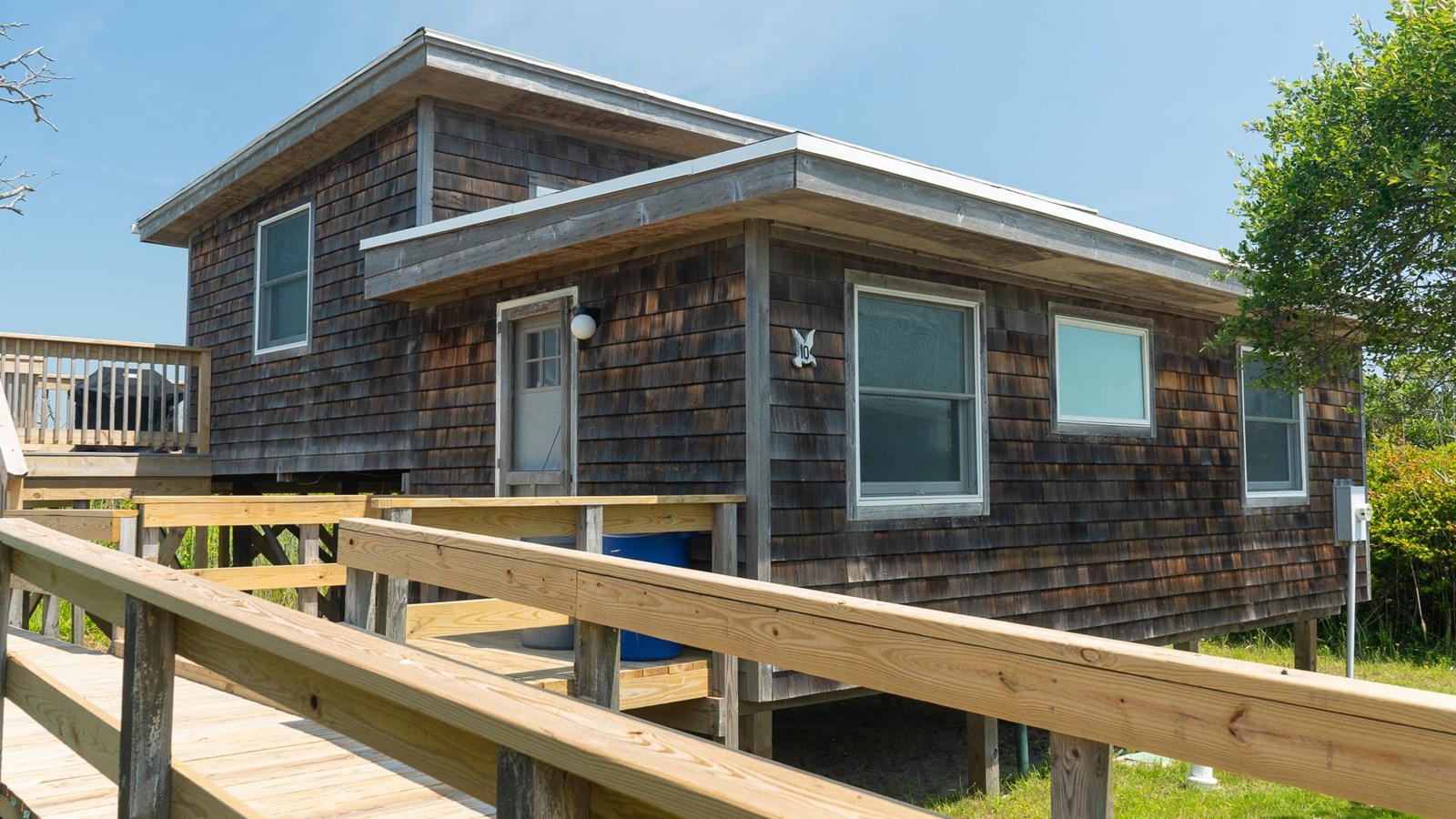 A wood-shingled raised beach house with surrounding decking.