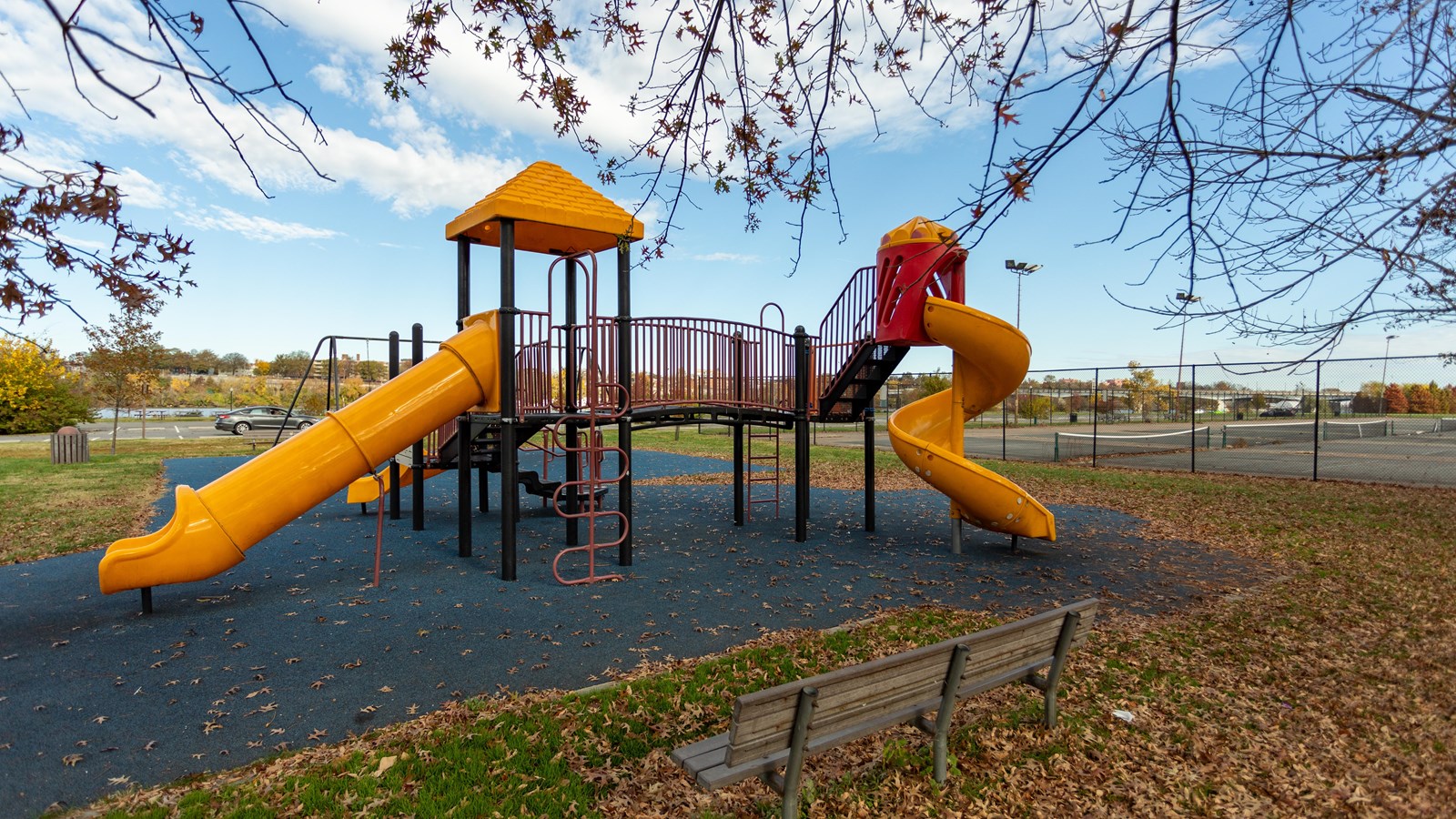 A playground area has three yellow slides and brown/orange railings. Tennis courts are in the back.