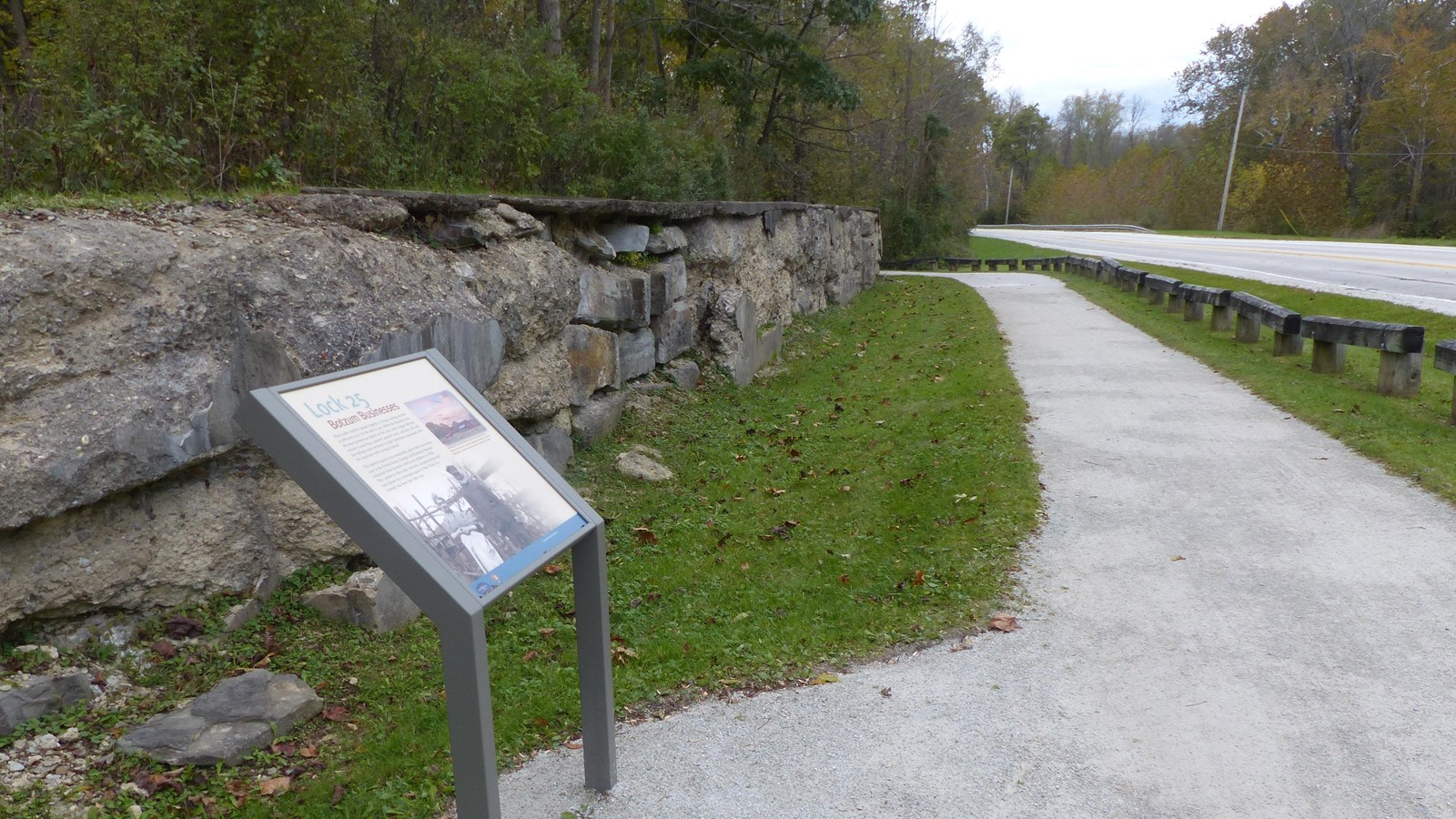 Exhibit panel faces a crumbling wall of large blocks and cement next to a gray trail.