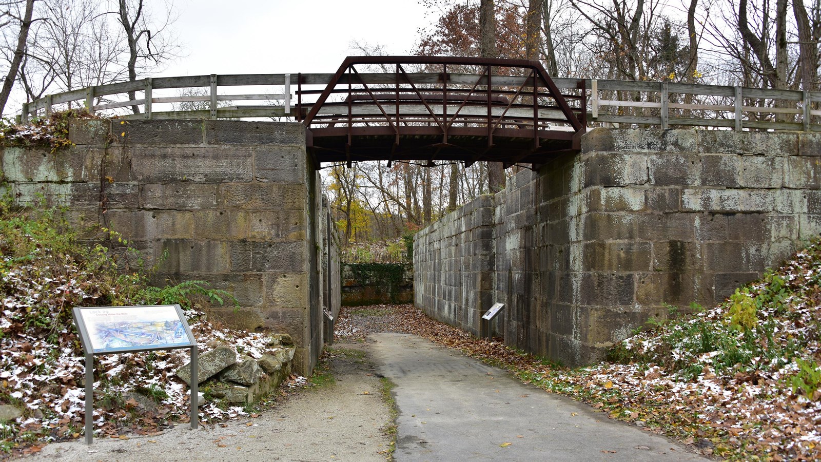 A trail bridge crosses over a path that leads inside a stone canal lock with exhibits.