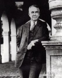 Man in suit leans against pole and poses for picture. 