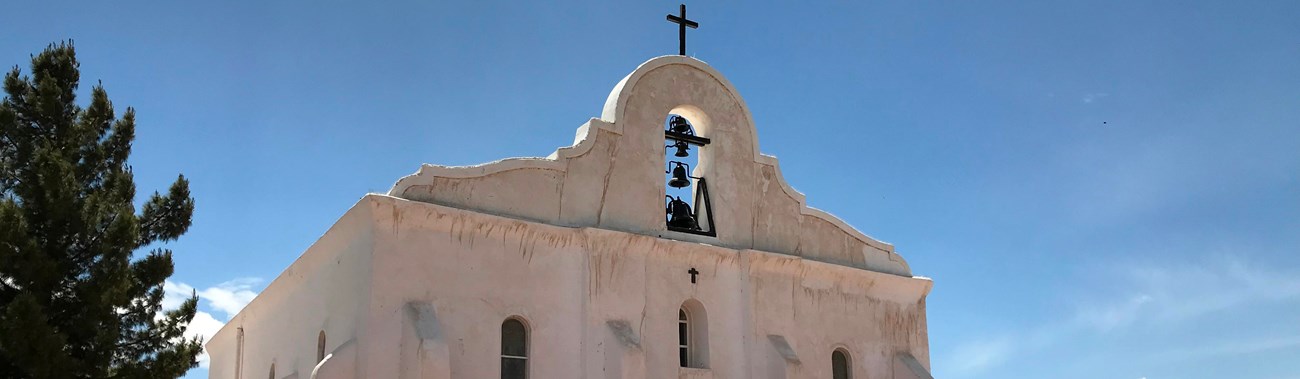 A tan, spanish-colonial style mission stands under a blue sky.
