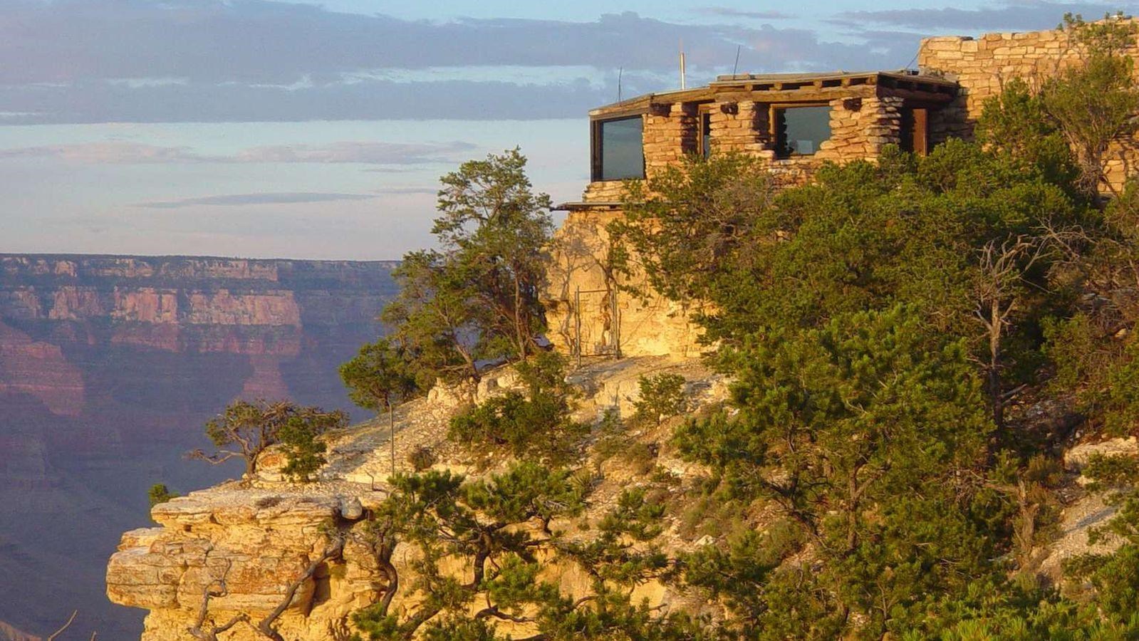 A rustic stone building with large windows on the edge of a cliff overlooking a canyon.