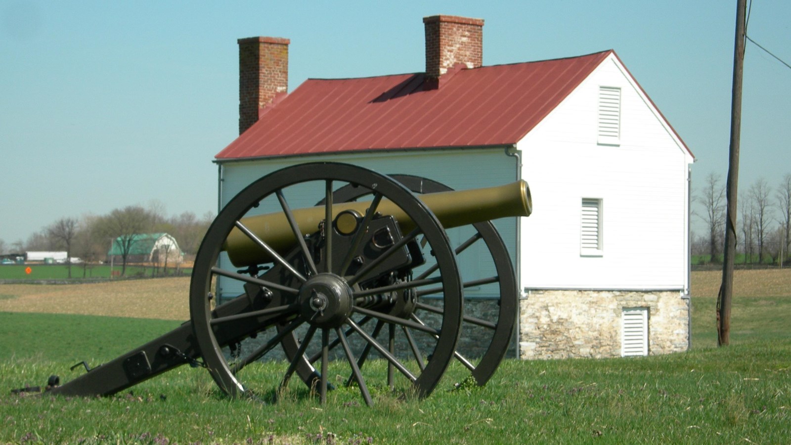 A replica Civil War cannon on a green lawn with a small white building behind it.