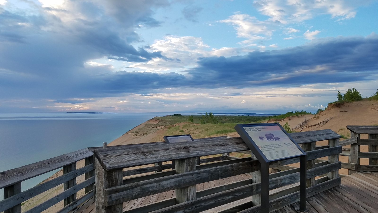 a wooden platform overlooks a sand dune descending to a large lake.