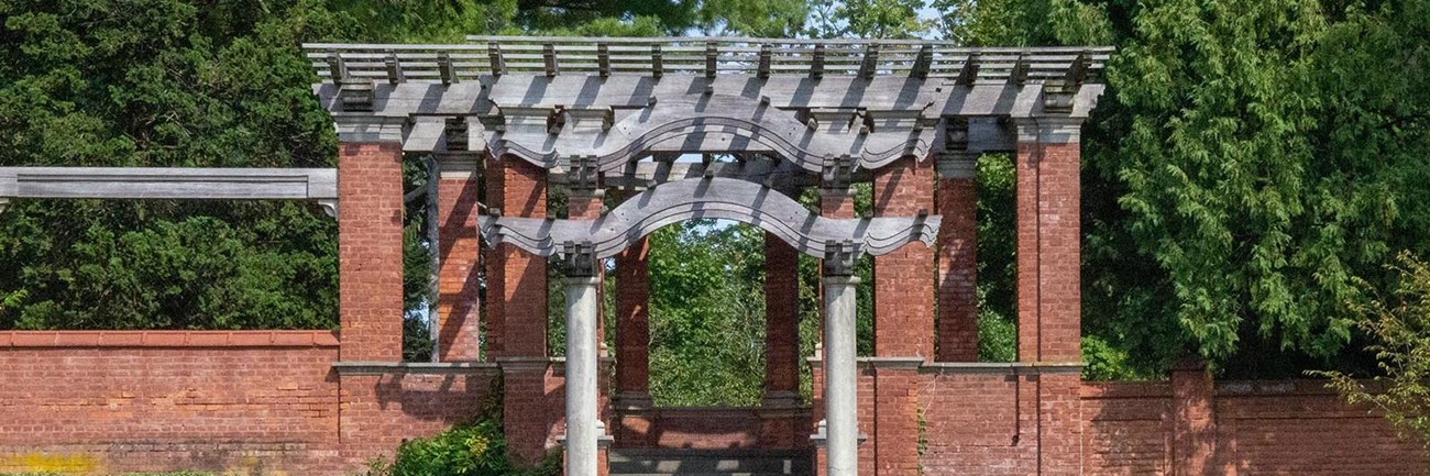 A white marble statue in a red brick pavilion before a reflecting pool.