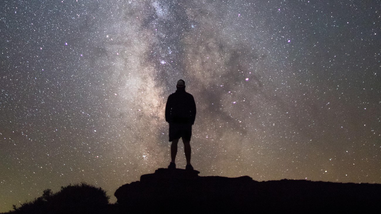 a person standing on a rock silhouetted against the milky way