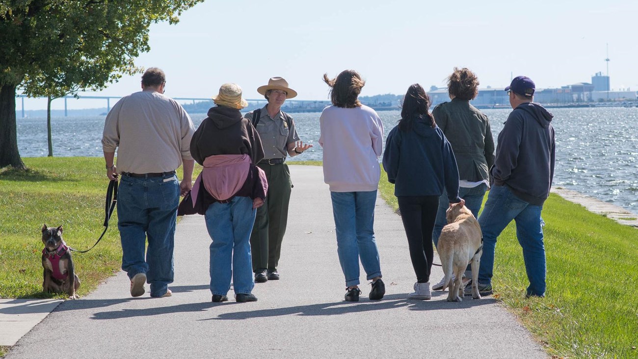 A ranger walking with visitors on the seawall trail. Several have dogs on leashes.