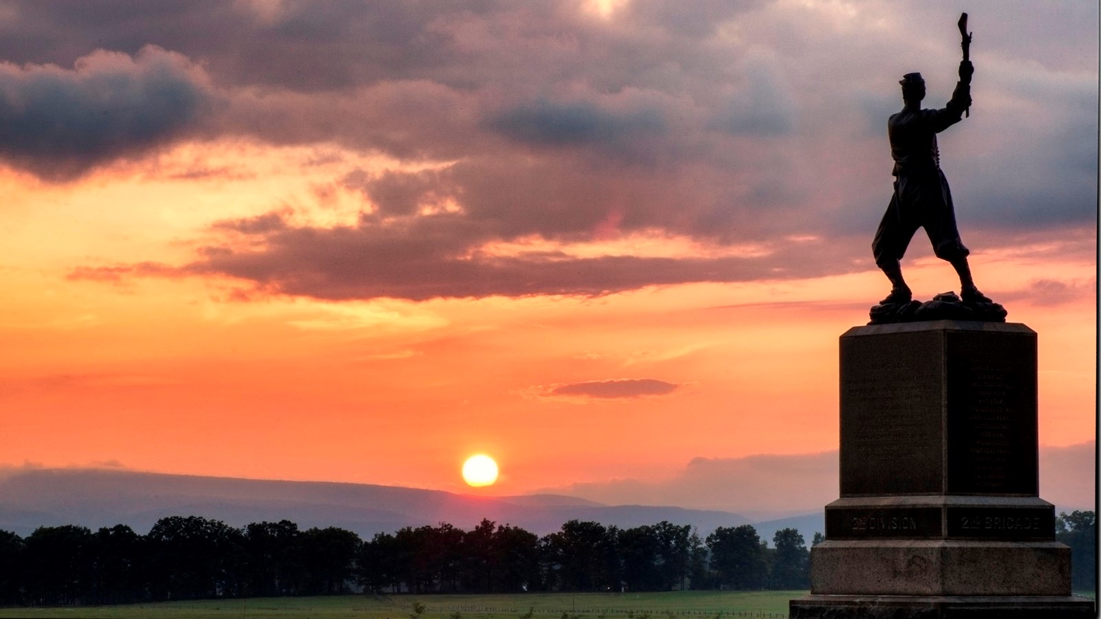 A bronze monument of a soldier overlooking a sunset