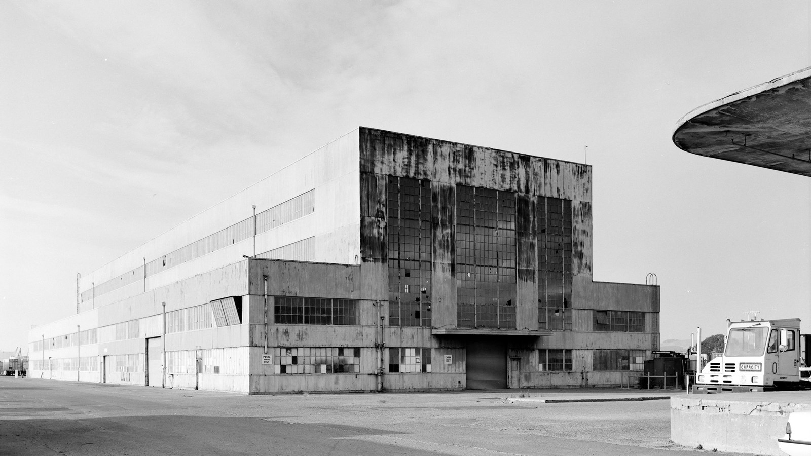 Historic photo of two-story building in shipyard. Large windows at front and surrounded by fence.