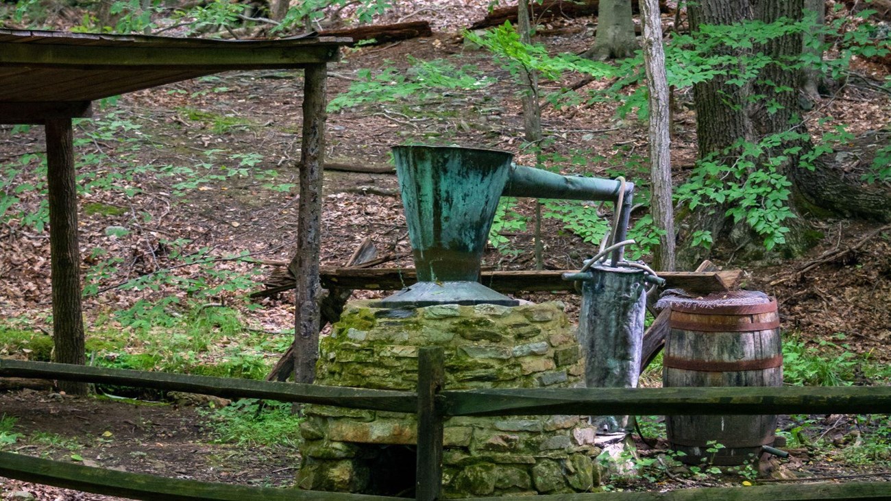 A stone oven with a metal caldron on top, draining into a wooden barrel. 
