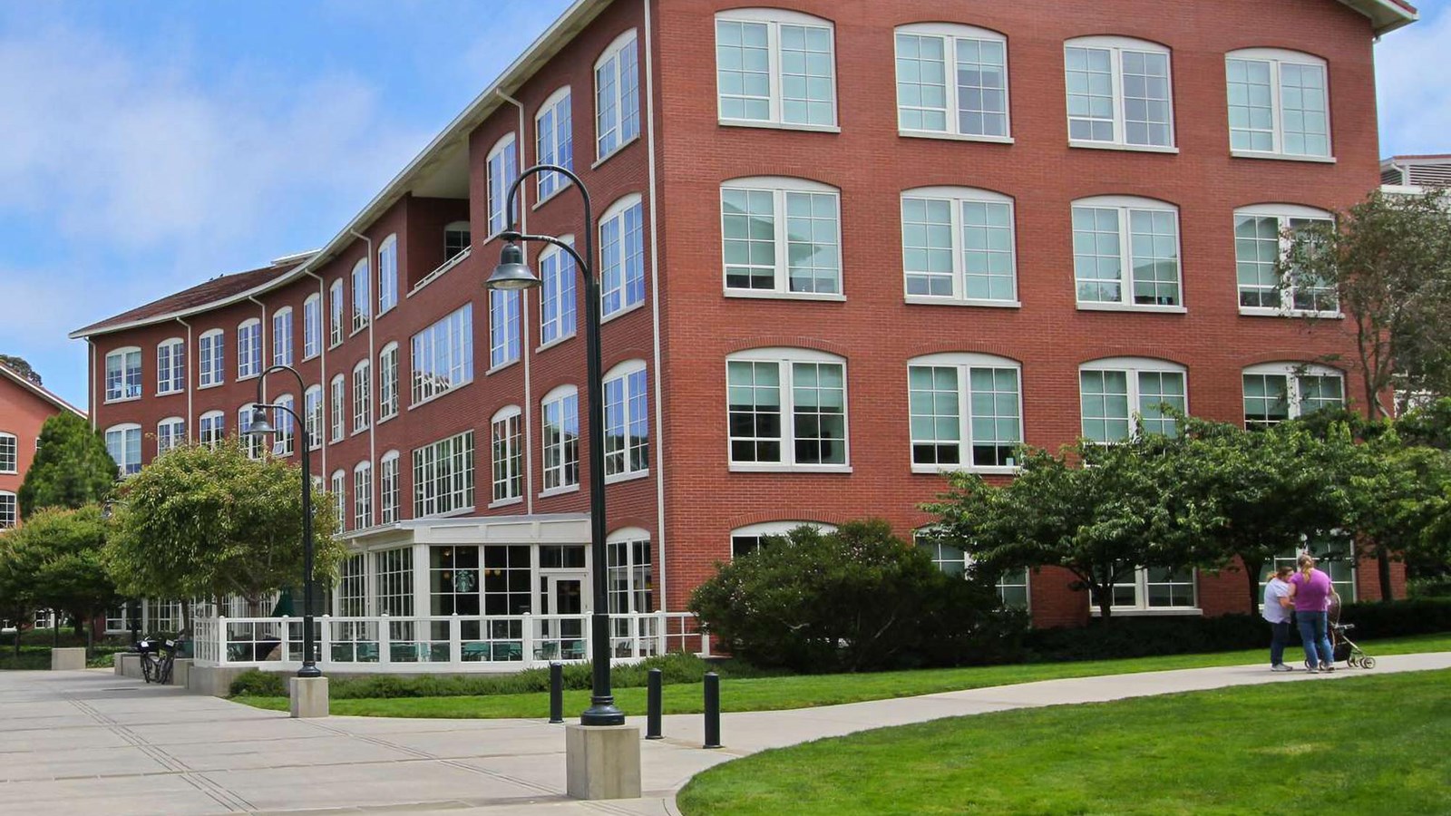 Multi story red bricked building with many windows and a patio at the base.
