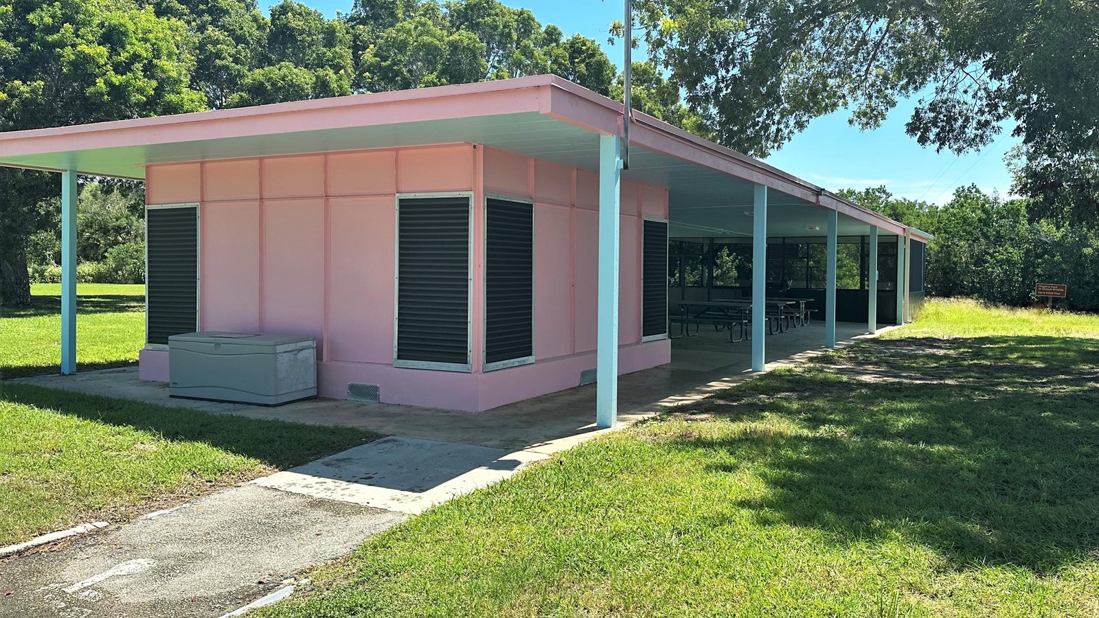A pink building with a screened-in porch filled with picnic tables.