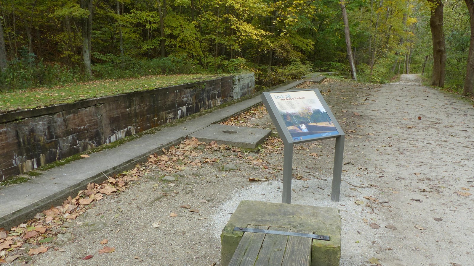 An exhibit panel and a bench are along the unpaved Towpath Trail, right, overlooking Lock 28, left.