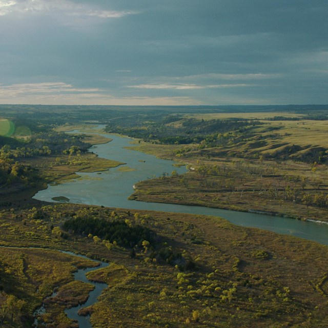 An aerial view of a blue-green river flowing through a green and gold valley.