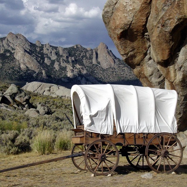 A covered wagon in front of a landscape of boulders and rocky outcroppings.