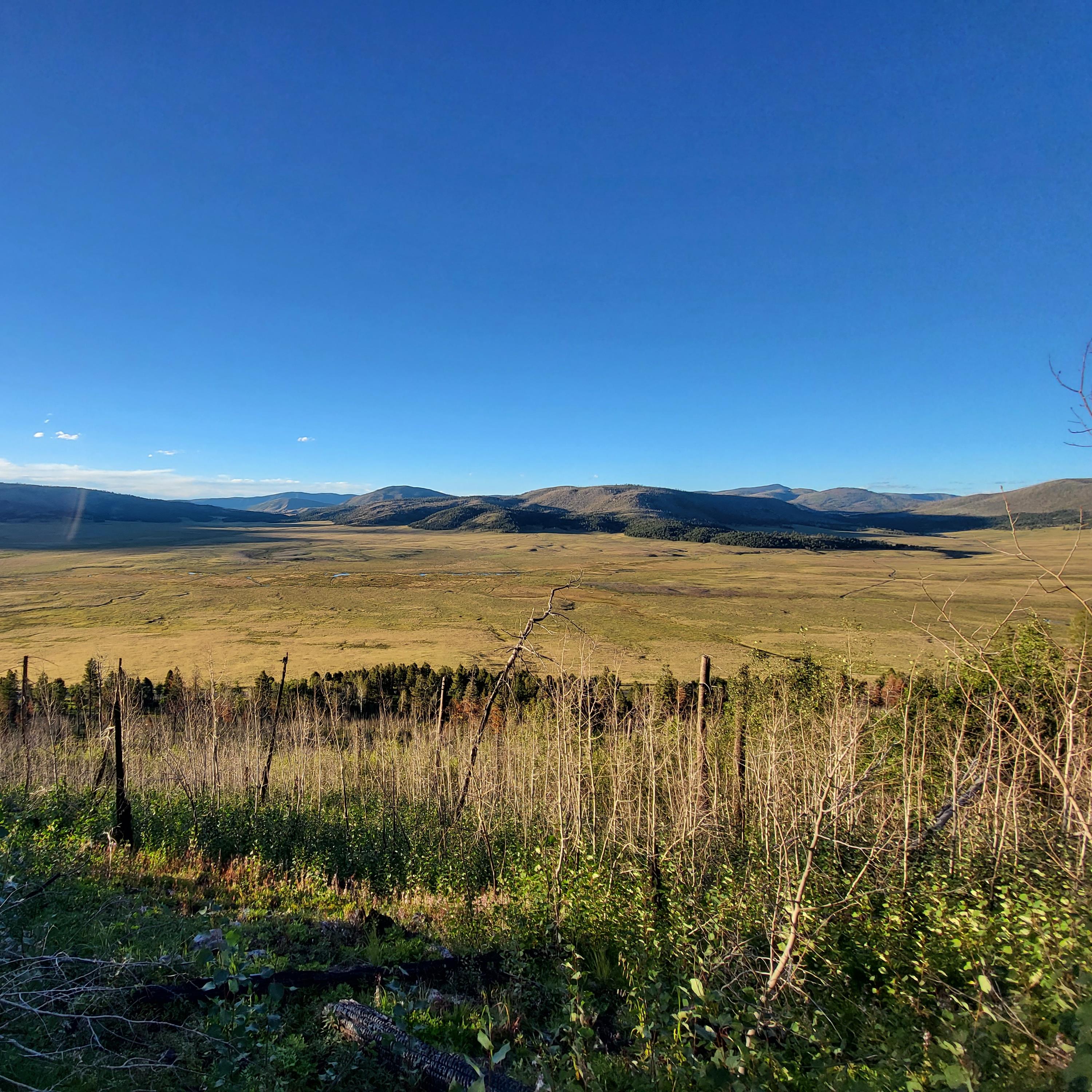 A view from a mountain into a large, grassy valley near sunset.