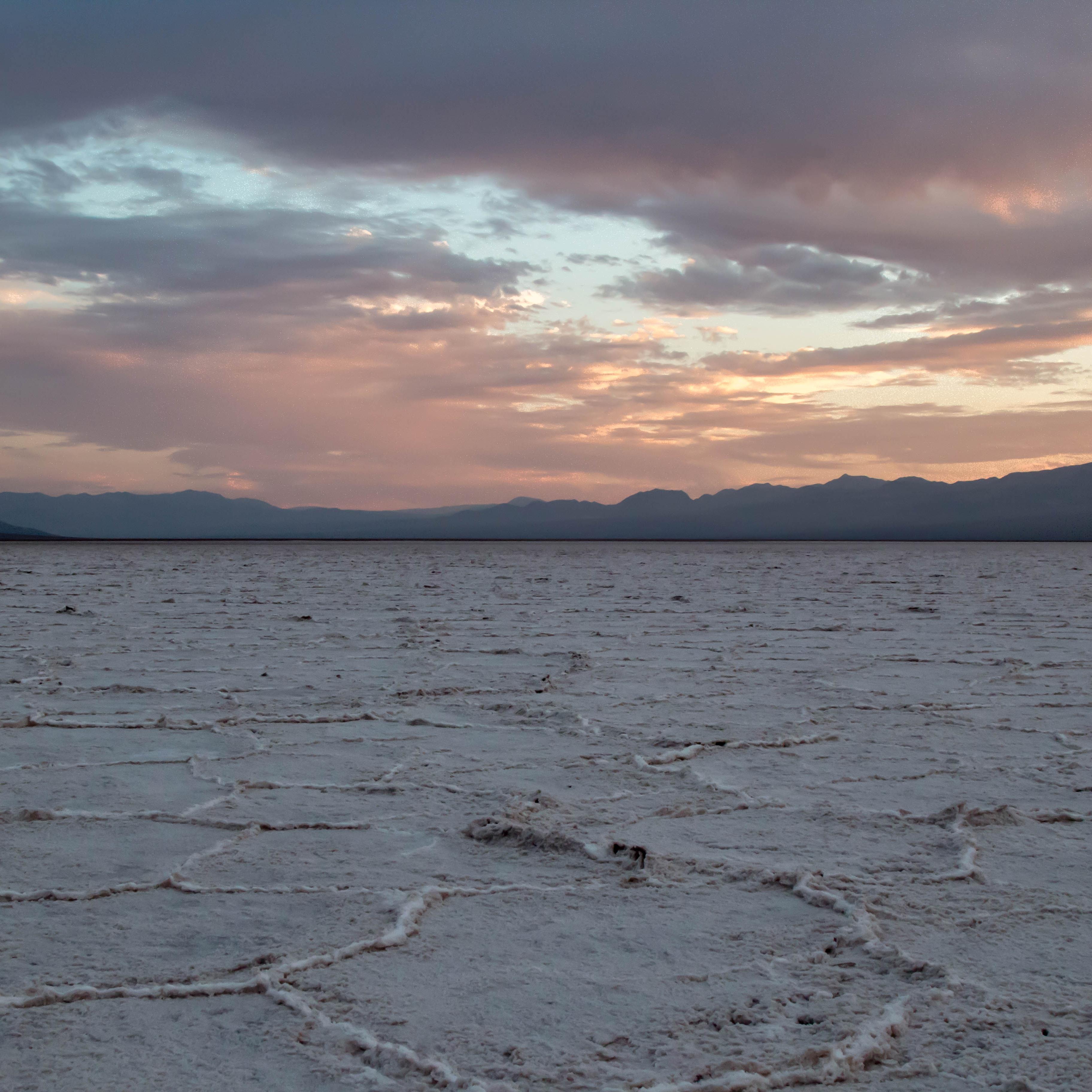 A vast salt flat stretches into the horizon with a cloudy sunset sky. 