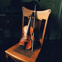 Violin and bow rests against wooden chair.